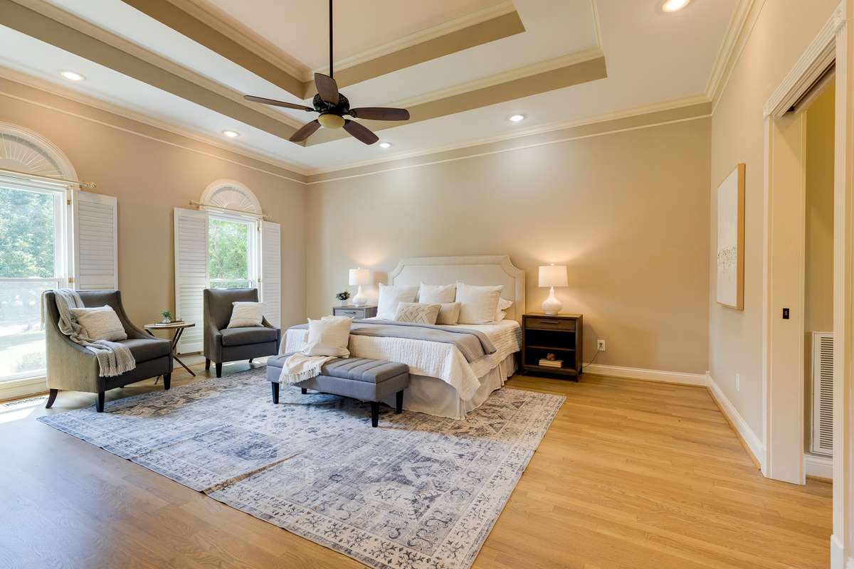 primary bedroom on ground floor with double tray ceiling and beautiful hardwood floors