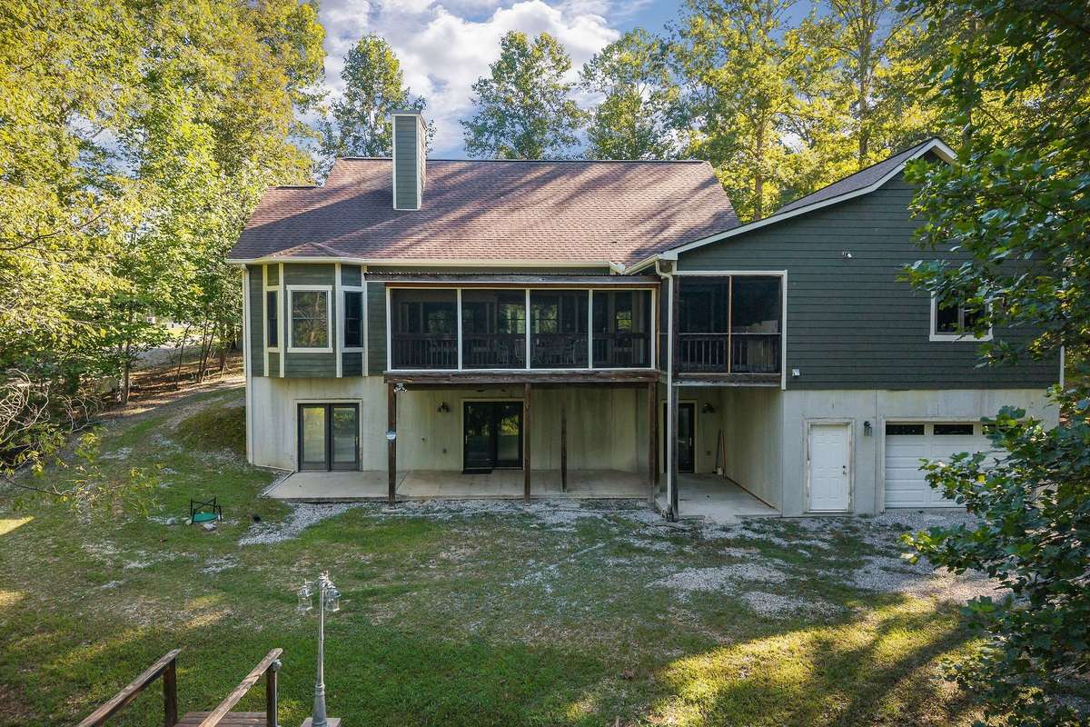 This view of the home showcases the bay window in the primary bedroom, the large screened-in back porch, and the patio area underneath the porch.