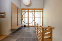 Light-filled interior gallery with slate flooring, custom wood detailing, and Shoji-style sliding doors creating a serene transition between levels.