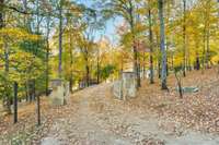 Gated, tree-lined private drive framed by mature hardwoods, highlighting the property’s private approach and seasonal landscape.