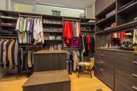 Custom-designed primary walk-in closet with built-in storage, drawers, display shelving, and center island.
