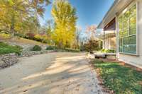 Side elevation and drive approach featuring stone retaining walls and mature trees.