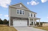 This beautiful front design features a combination of stone accents, Hardie board siding, and decorative shaker board, offering timeless curb appeal. A covered front porch adds a welcoming touch and the perfect spot to enjoy a quiet moment outdoors.