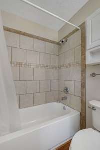 The Primary Bedroom's full bath features a combo bathtub & shower, surrounded by beautiful decorative tile.