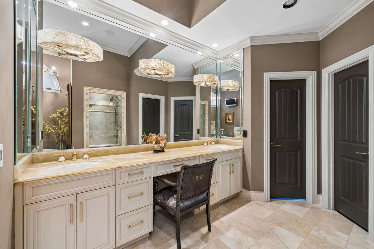 Honey onyx dual sink vanity with uplighting, custom beveled framed mirror and lighting. Double closets.