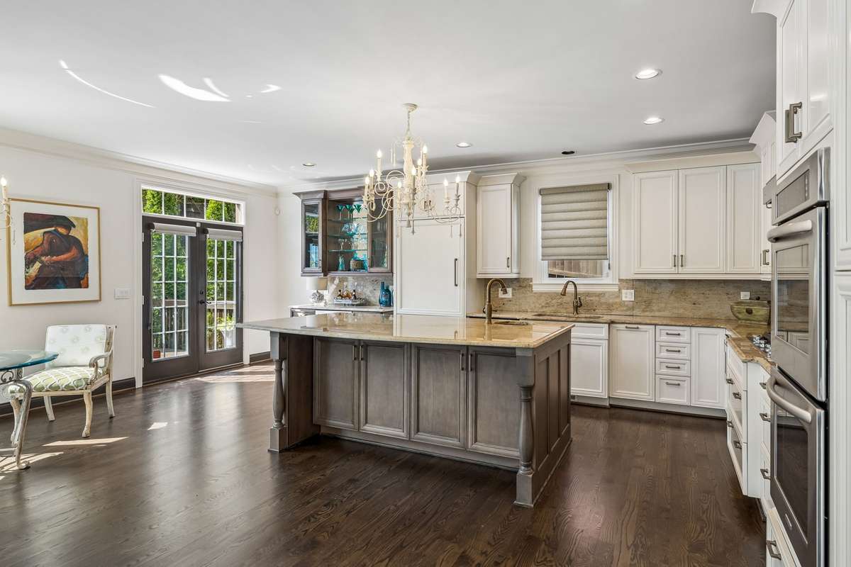 Granite countertops and backsplash, designer chandeliers, Hunter Doulas woven vignette Roman shades. French doors lead out to wood deck.