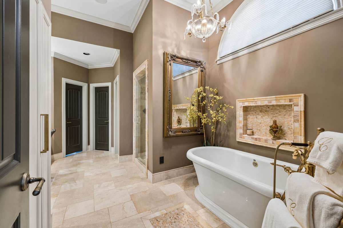 Primary bathroom has travertine floors, honey onyx inlays, free standing soaker tub, separate shower, dual sink vanity, and designer lighting.