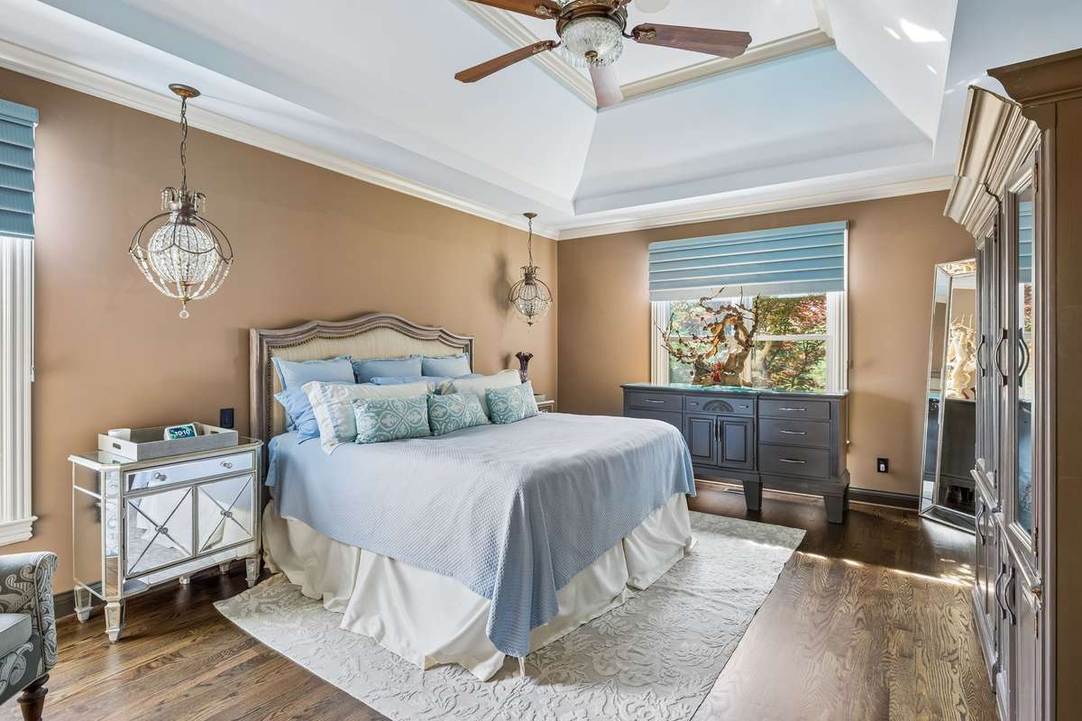 First floor primary suite with trey ceiling and custom crown molding. Bedside ceiling hanging designer light fixtures and 52" ceiling fan. Hunter Douglas luminette shades.