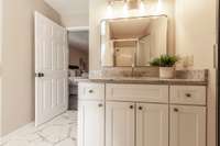 White cabinetry in the bathroom offers a clean, timeless look with ample storage space. Granite countertops add a touch of luxury and durability to the updated bathroom.