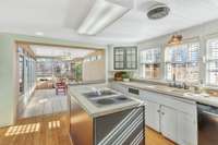 Island with electric cooktop, double bowl sink with gooseneck faucet, stainless steel refrigerator, and wall oven.