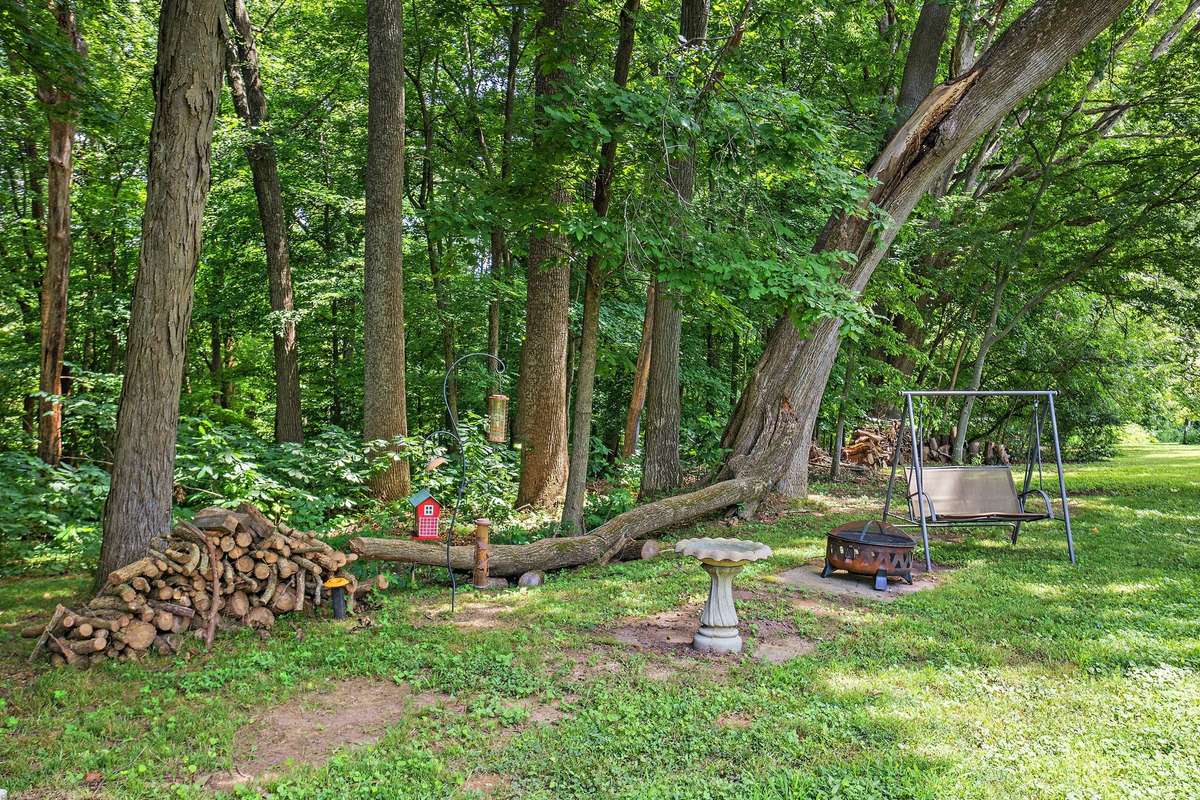 A peaceful wooded spot providing space for outdoor relaxation, with room to arrange seating or a firepit as desired. Mature trees create a natural, shaded retreat within the backyard setting.