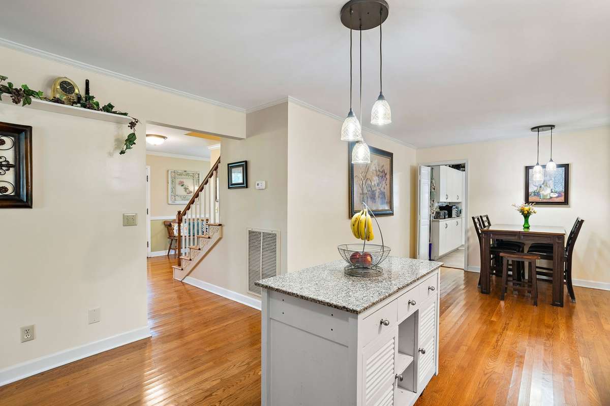 Open kitchen view featuring hardwood floors, pendant lighting, and a granite-top island. The space flows into the eat-in area and foyer, creating a functional layout connecting the home’s main living spaces.