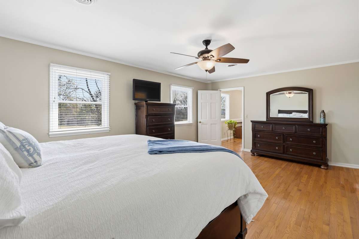 Primary Bedroom (Alternate View) – This bright and spacious primary bedroom offers multiple windows that fill the space with natural light, complemented by warm hardwood flooring and neutral tones. Generous layout provides room for additional furnish