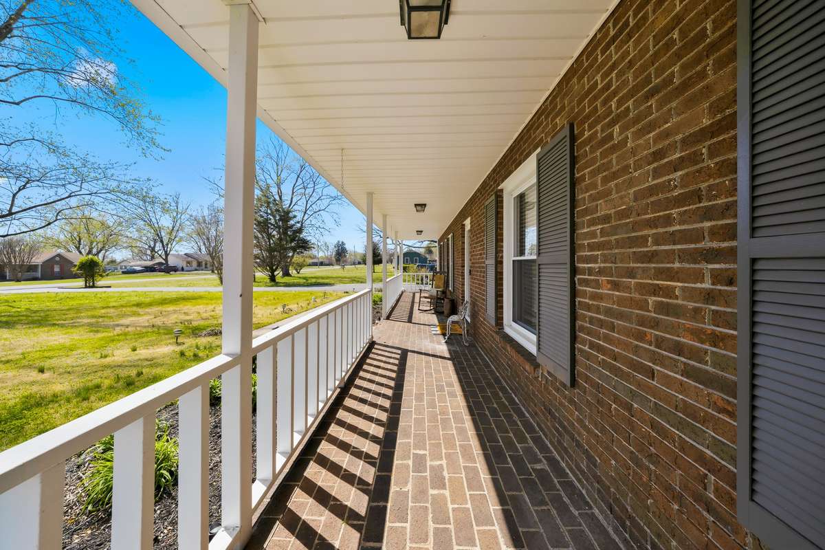 Front Porch (Alternate View) – Extended porch offers plenty of room for rocking chairs or décor, with charming brick details and a shaded setting perfect for morning coffee or evening unwinding.