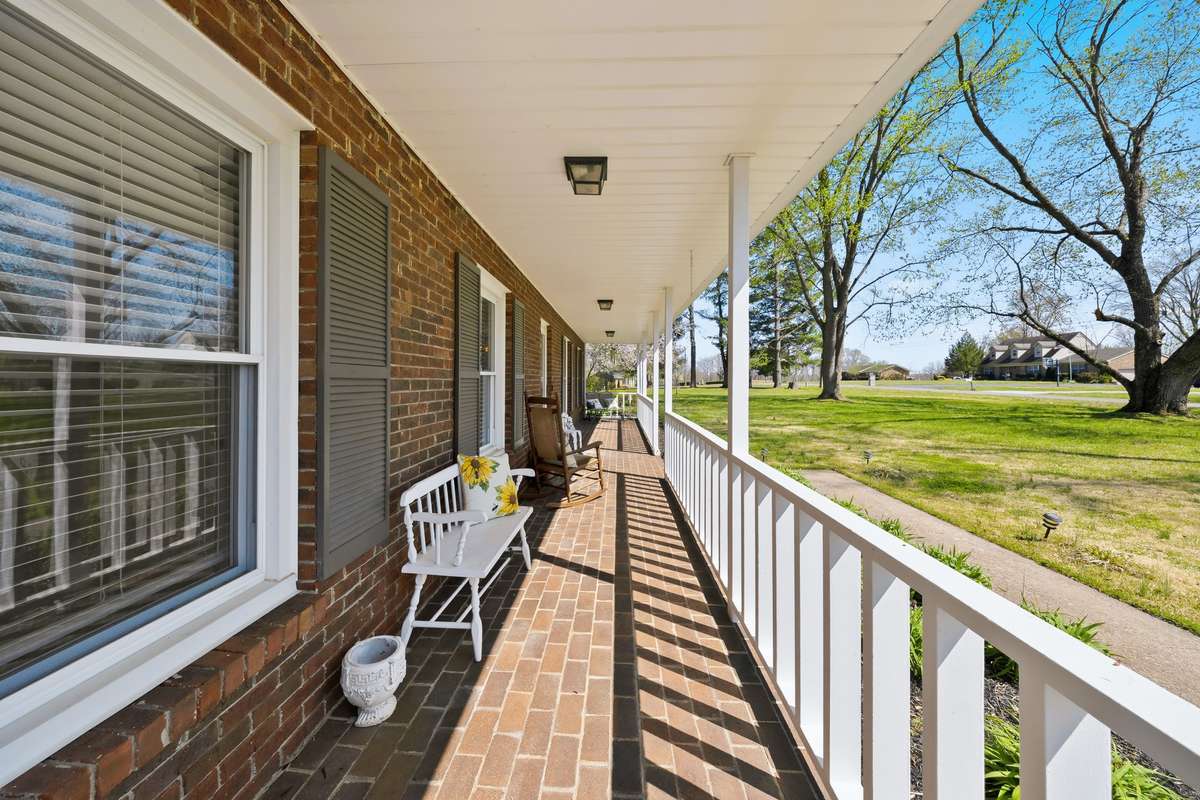 Front Porch – Welcoming covered front porch with classic brick flooring, white railings, and ample space for seating. Ideal for relaxing outdoors while enjoying views of the front yard.