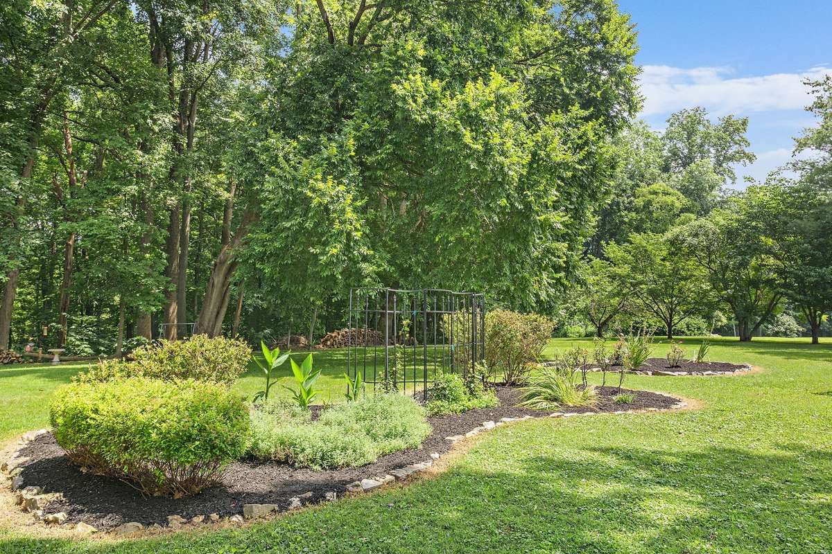 Beautifully designed garden beds with stone borders, shrubs, and flowering plants add visual interest to the expansive yard. The surrounding tree canopy provides shade and a serene outdoor environment.