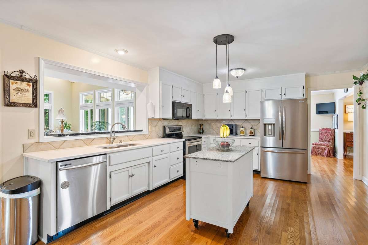 The bright and functional kitchen offers abundant cabinetry, stainless steel appliances, and a central island for extra workspace. A wide pass-through window overlooks the living area, enhancing flow and connectivity.