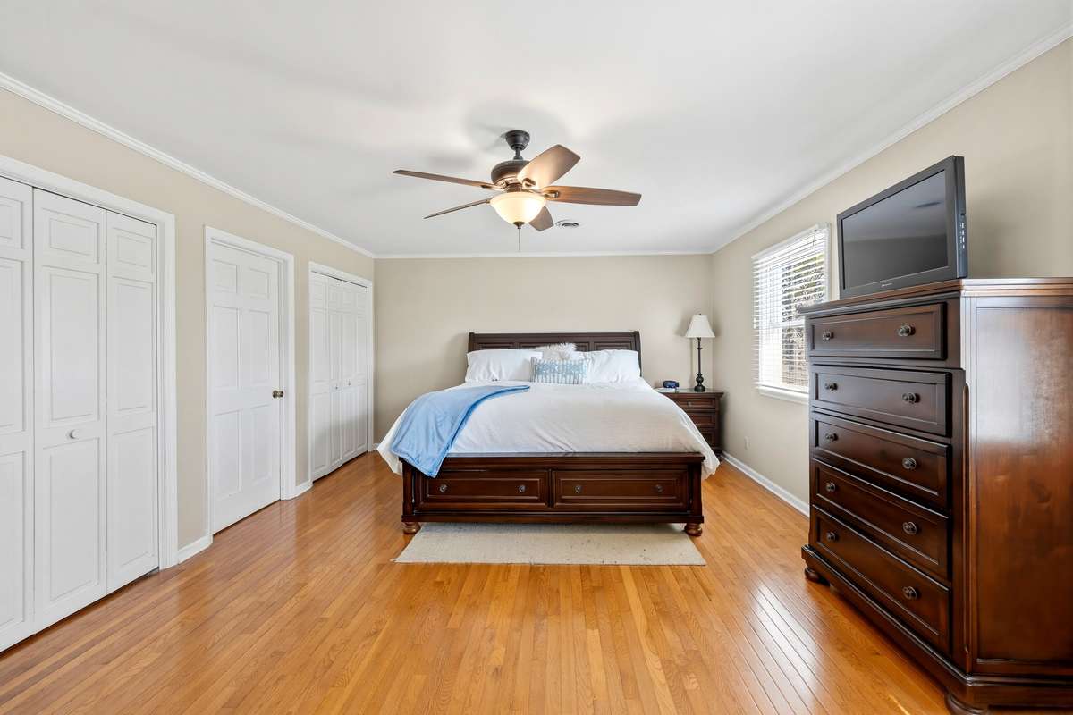Primary Bedroom – Spacious and inviting bedroom featuring warm hardwood flooring, a large window for natural light, and a ceiling fan for added comfort. Dual closets provide ample storage, while the layout easily accommodates full furniture sets for