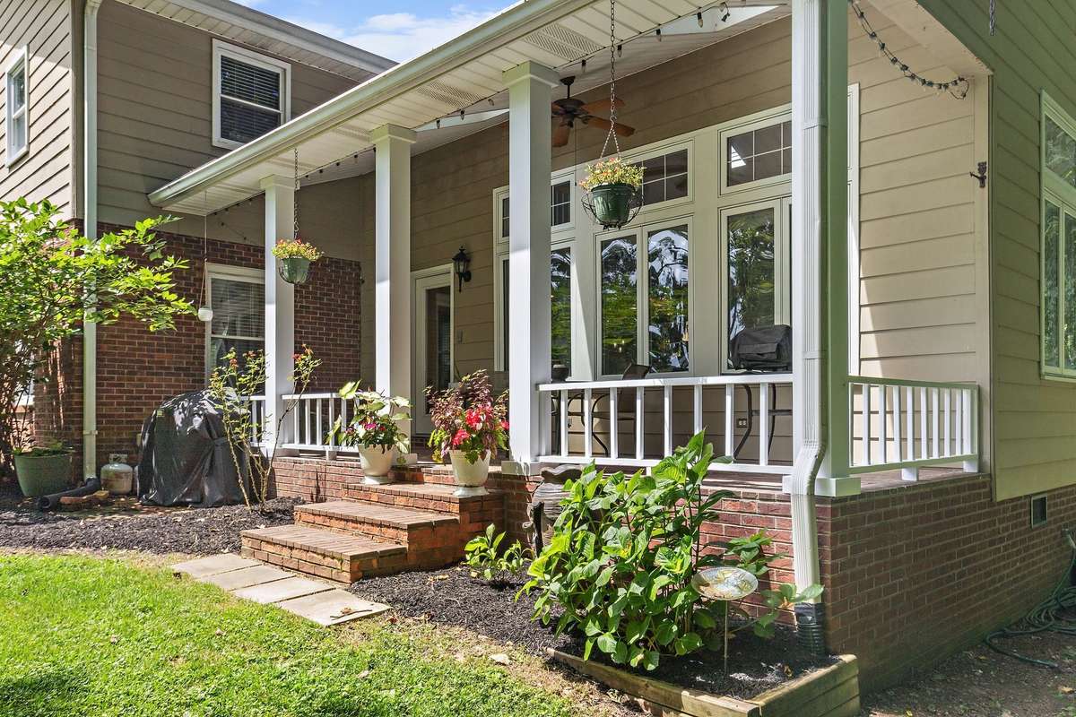 A closer view of the side porch showcases the steps, decorative planters, and ample outdoor living space. The brick and siding exterior blends seamlessly with the landscaped garden beds.