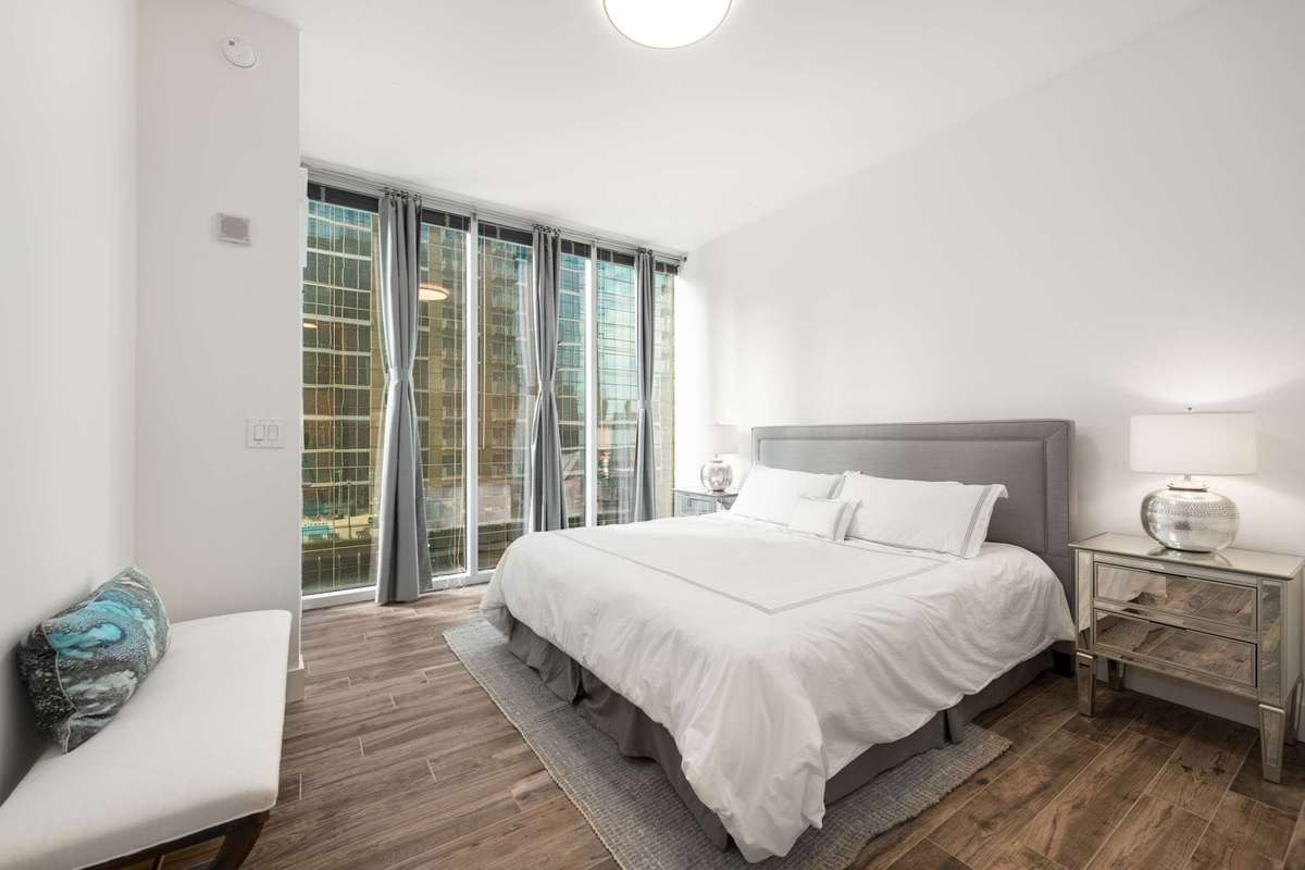 Spacious primary bedroom with floor to ceiling glass and fresh lighting.