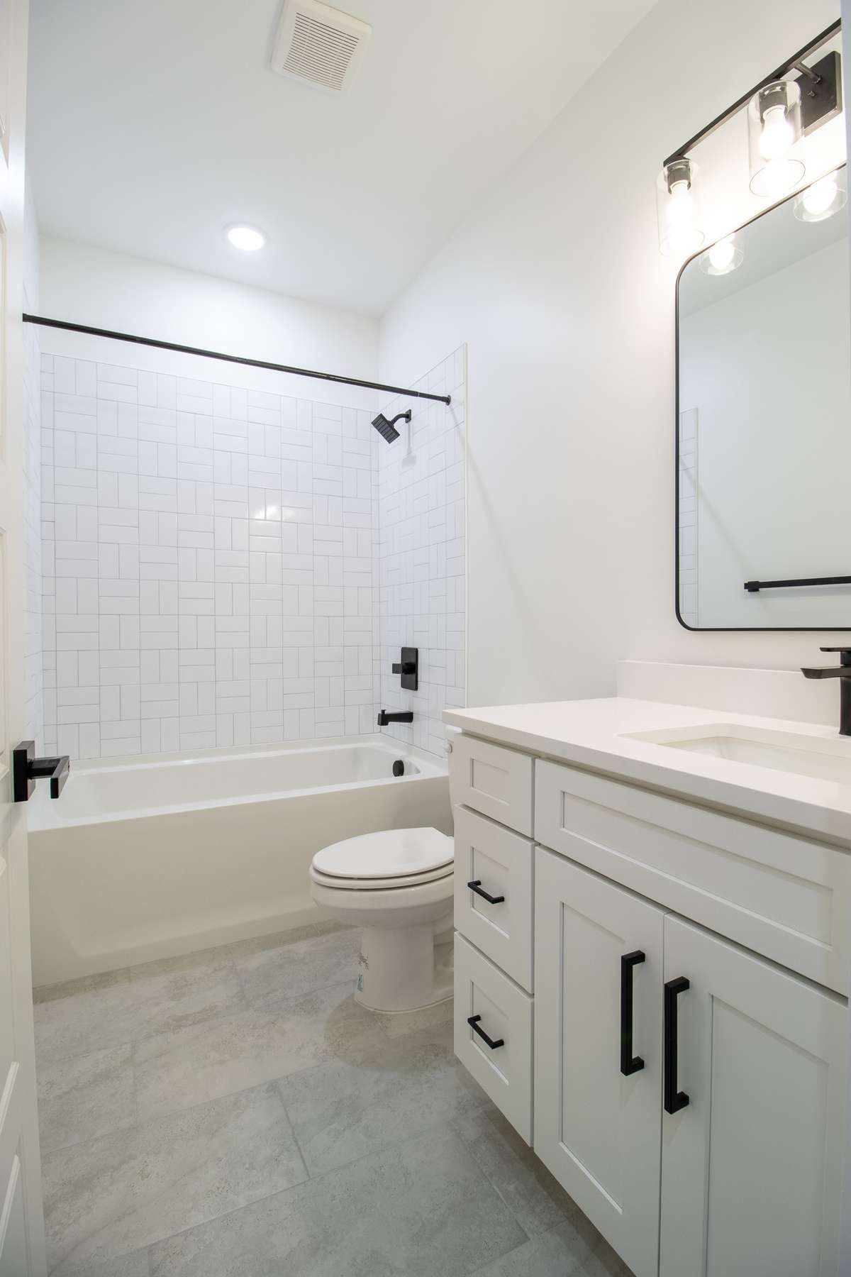 The secondary bath has modern tile and classic white cabinets with quartz counter tops and matte black accents.