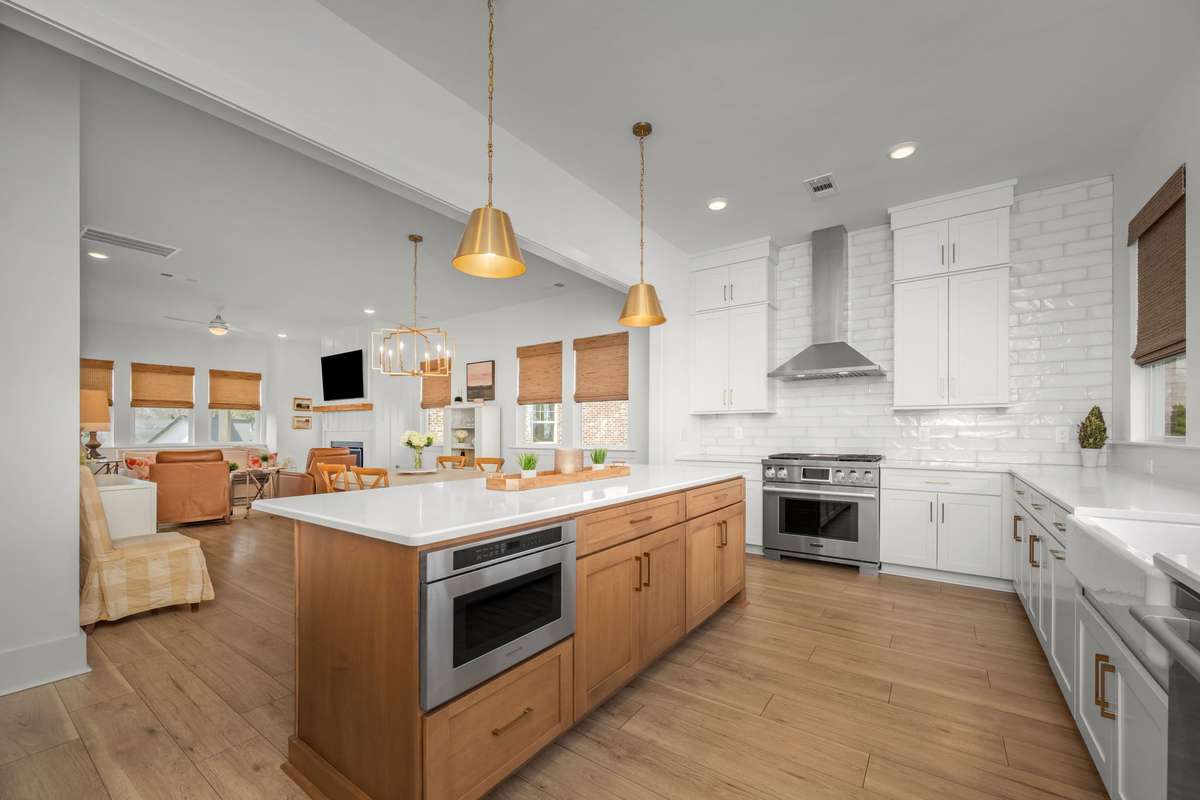 Gourmet kitchen with oversized island, quartz counters, gas range with stainless vent hood, custom backsplash, picturesque windows, and a hidden walk-in pantry!