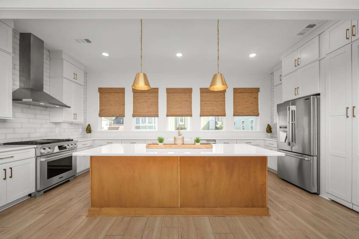 Gourmet kitchen with oversized island, quartz counters, gas range with stainless vent hood, custom backsplash, picturesque windows, and a hidden walk-in pantry!