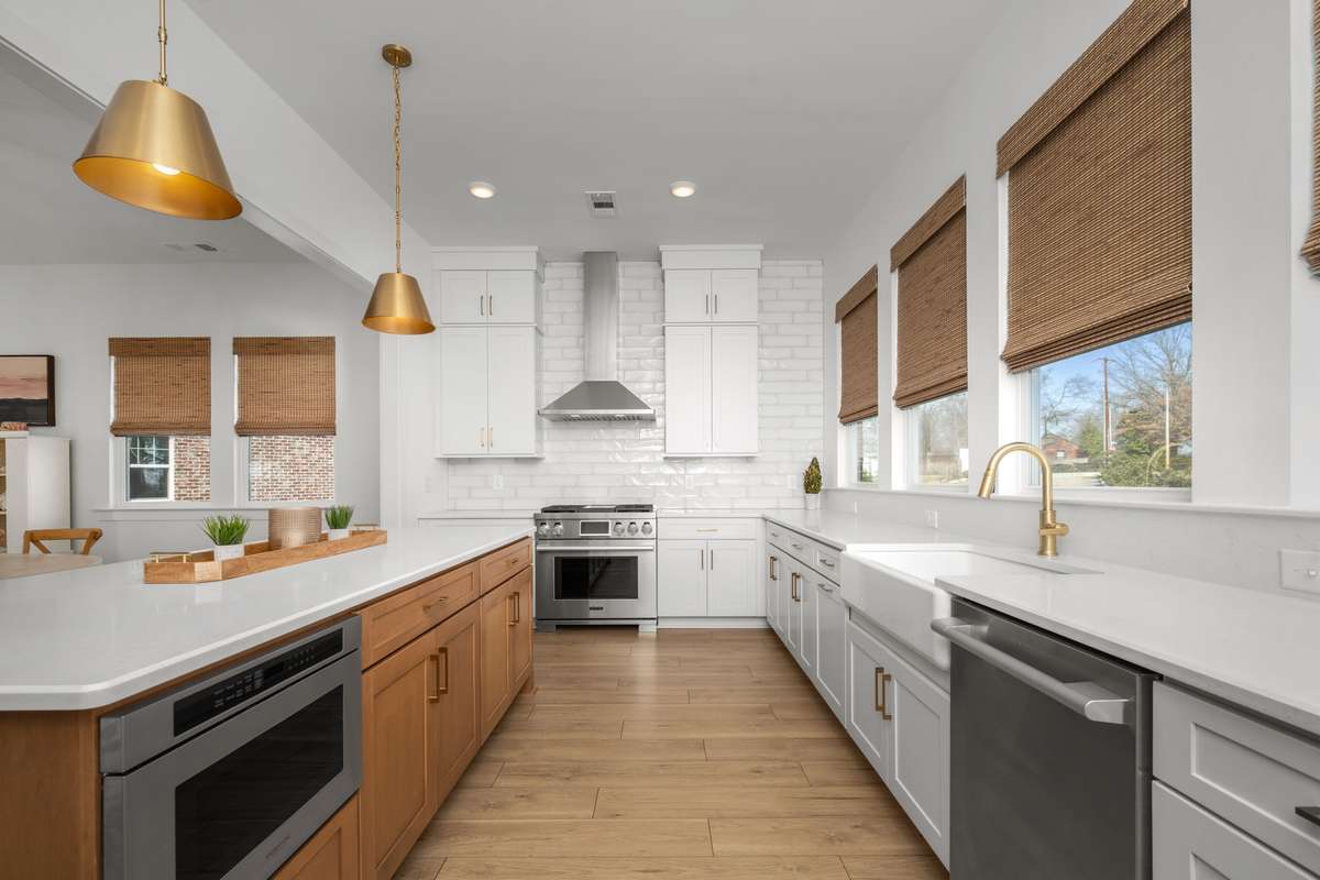 Gourmet kitchen with oversized island, quartz counters, gas range with stainless vent hood, custom backsplash, picturesque windows, and a hidden walk-in pantry!