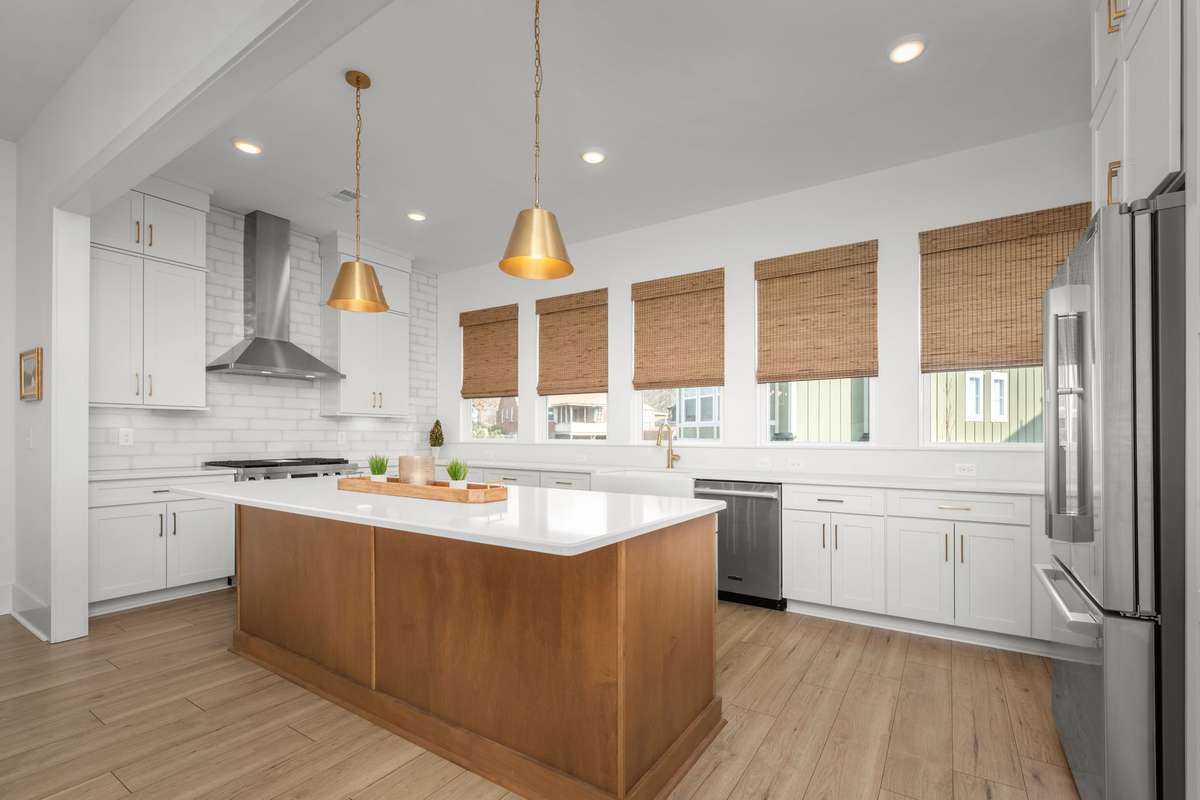 Gourmet kitchen with oversized island, quartz counters, gas range with stainless vent hood, custom backsplash, picturesque windows, and a hidden walk-in pantry!