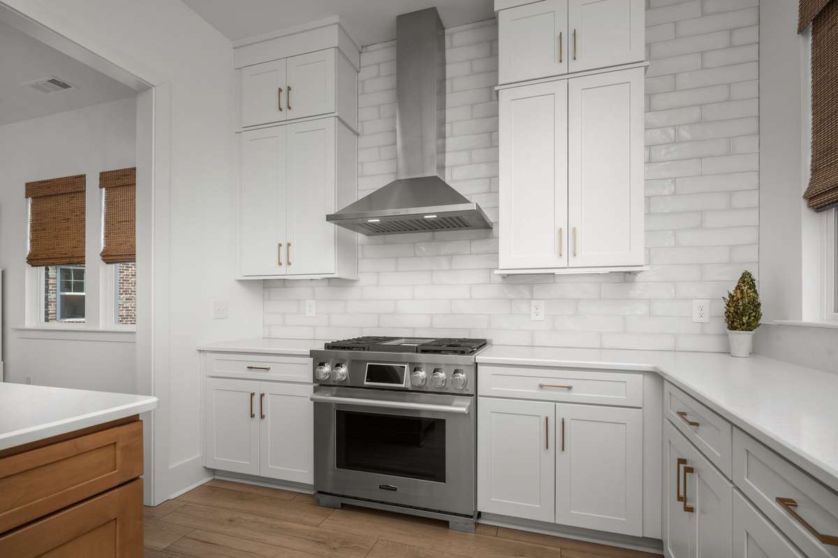 Gourmet kitchen with oversized island, quartz counters, gas range with stainless vent hood, custom backsplash, picturesque windows, and a hidden walk-in pantry!