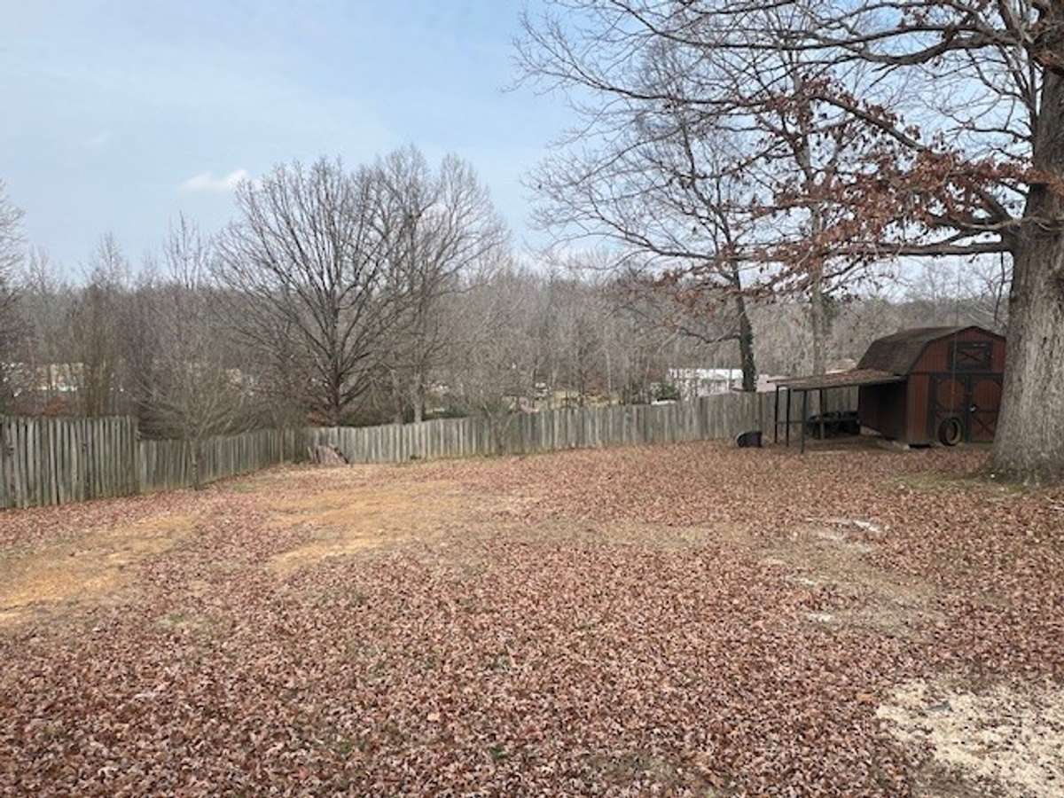 Large back yard with shade trees and storage building.