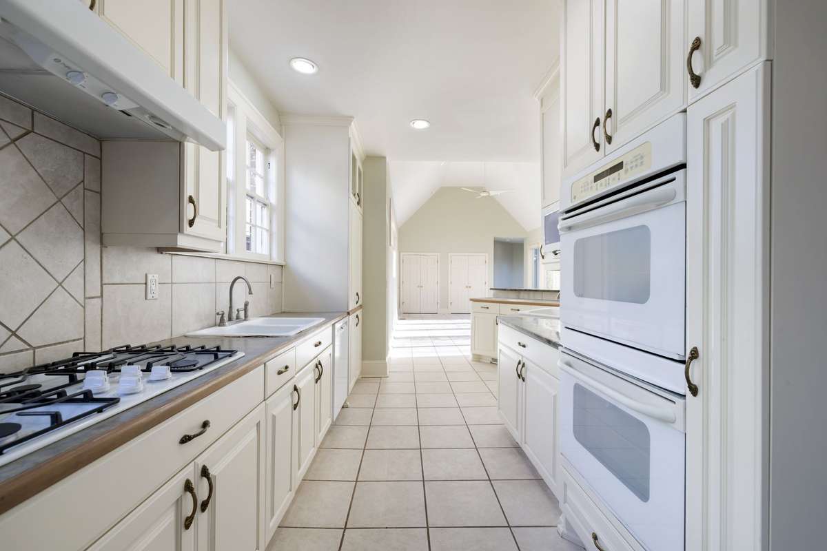 Bright kitchen layout features GE double wall ovens, recessed lighting, and direct sightlines to the expansive sun room.
