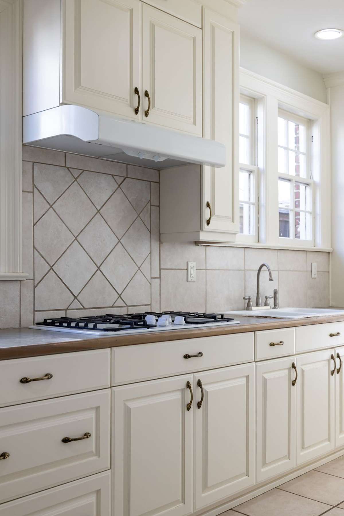A diamond-patterned backsplash matches the Tudor aesthetic, highlighting a gas cooktop and ample storage.