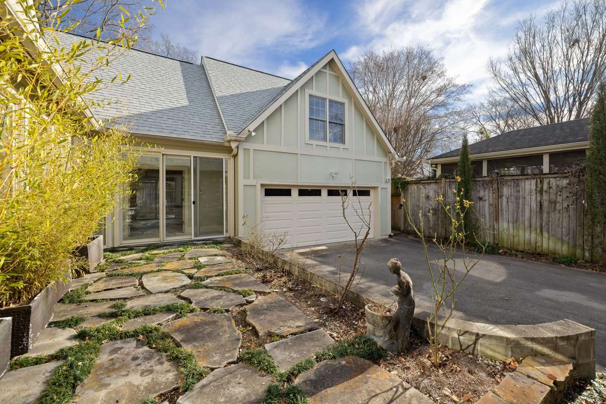 Glass doors open to a cozy, stone-paved outdoor space. An apartment above the two-car garage overlooks the area.
