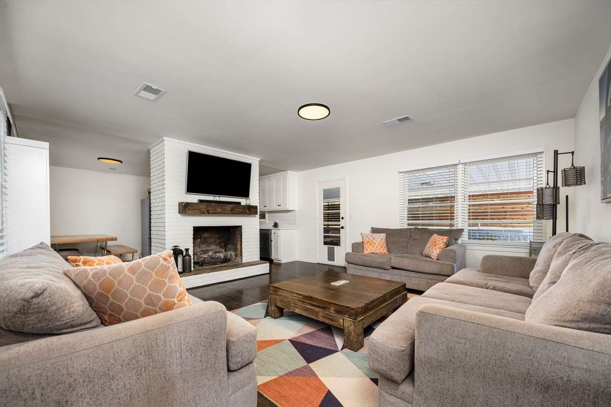Spacious living room with a white brick fireplace, hardwood floors, and large windows for natural light.