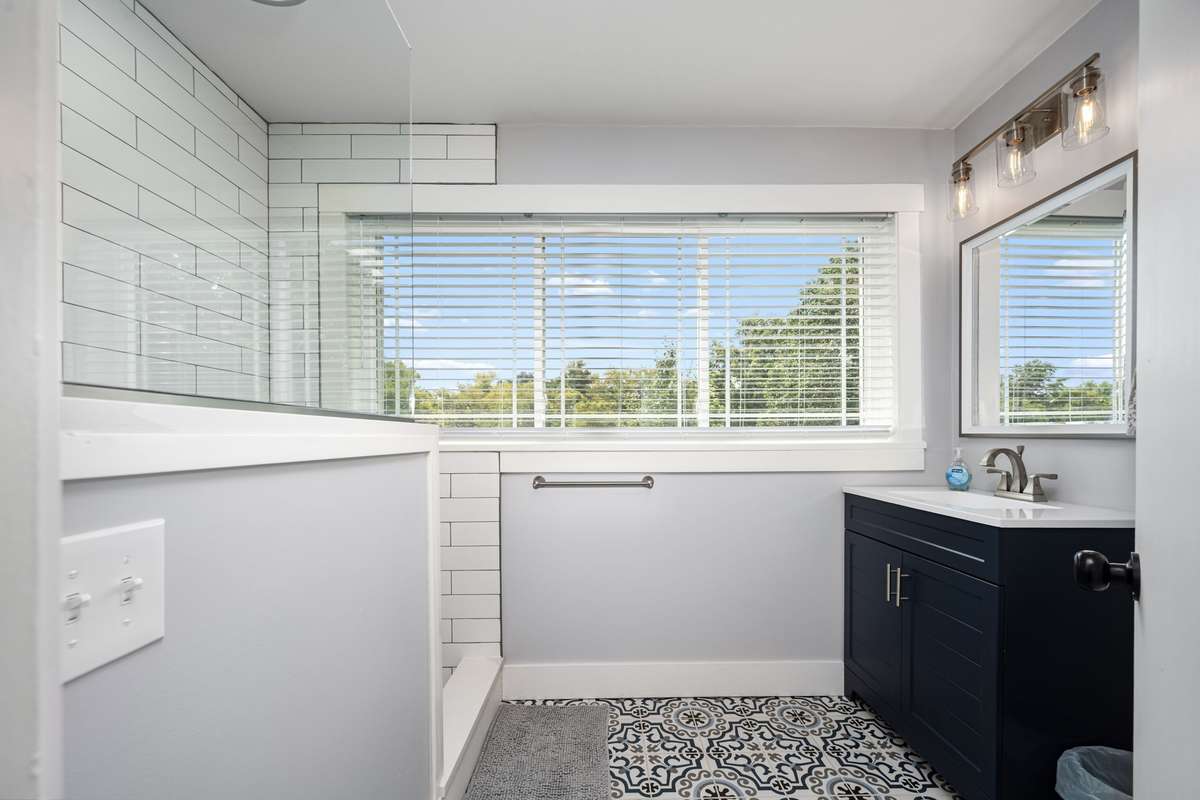 Updated secondary bathroom located off the flex room features patterned tile flooring, subway-tile shower surround, and a sleek navy vanity with modern lighting.