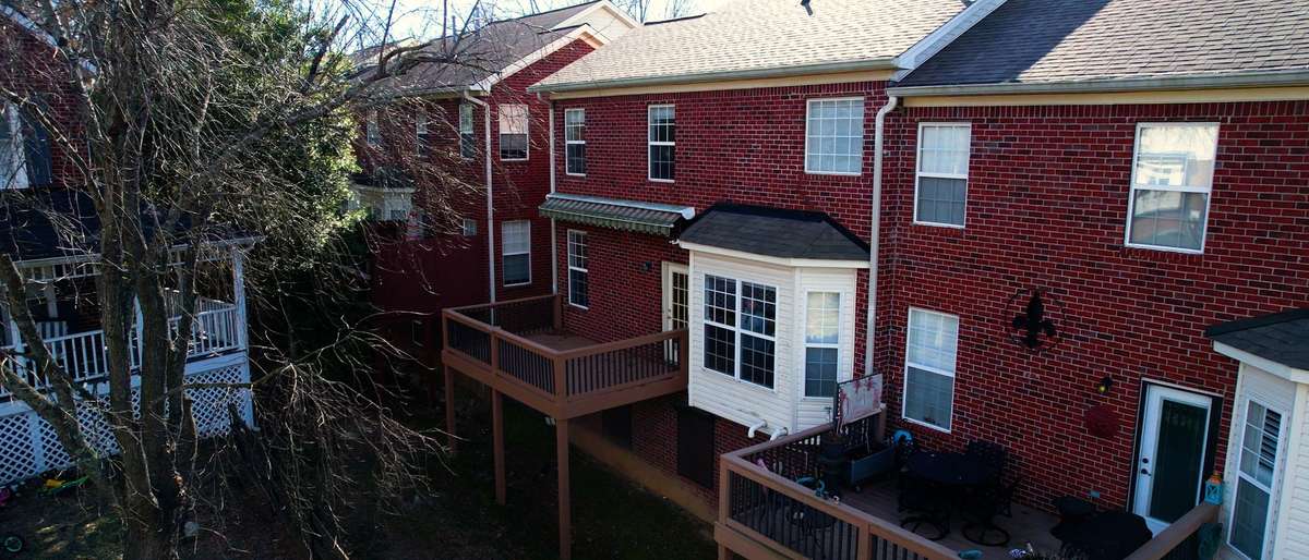 From the back of the townhome you can see the deck with the closed awning, bay window as well as the basement bonus room with the storm shutters in the closed position.
