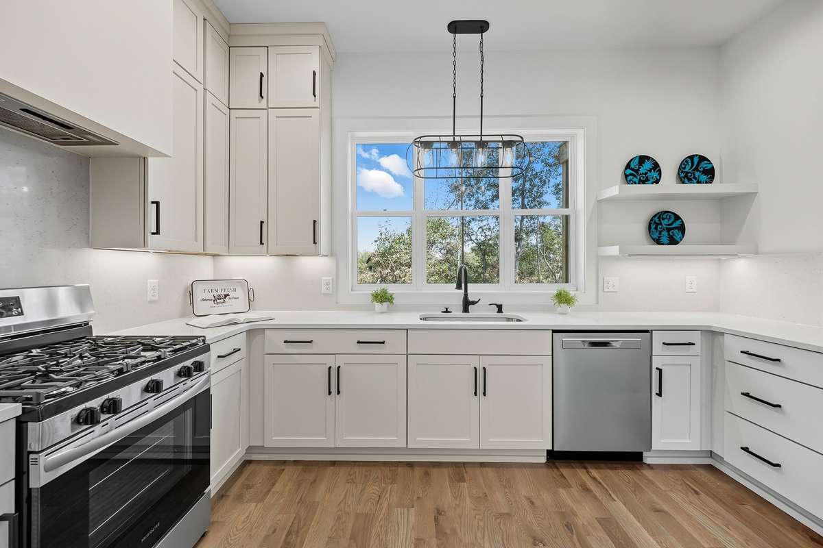 Bright kitchen with shaker cabinetry, stainless steel appliances, and quartz countertops with a overview of the backyard and river while preparing food for your guests.