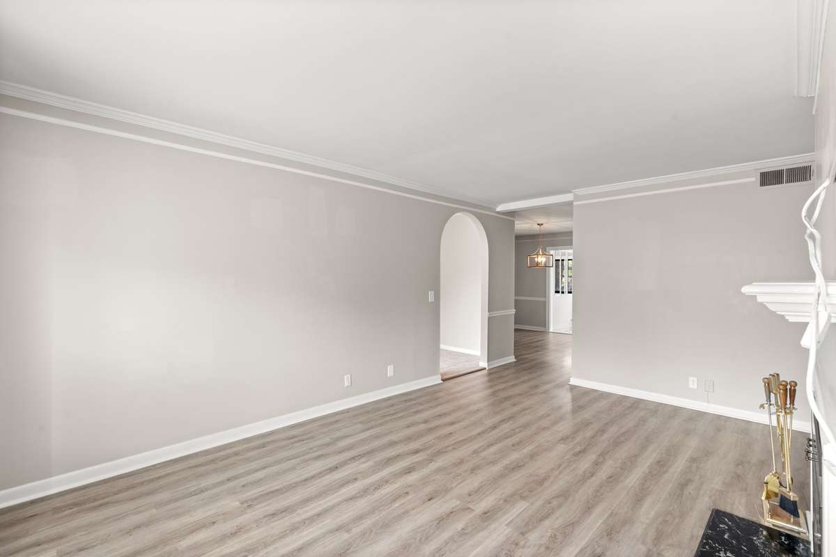 Spacious Living Room with a wood-burning fireplace, fresh paint, lots of natural light, and LVP flooring. Ached doorway and crown moulding offer an elevated feel to this peaceful space.