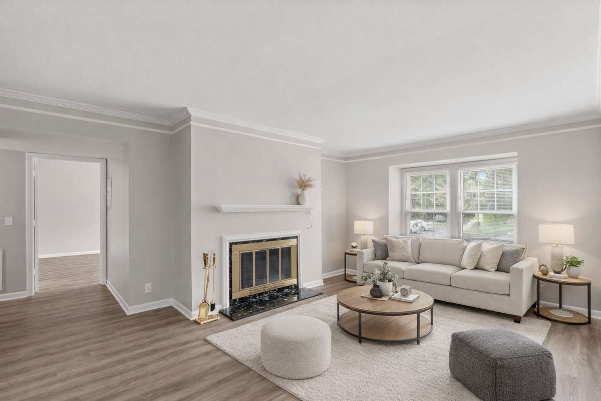 Spacious Living Room with a wood-burning fireplace, fresh paint, lots of natural light, and LVP flooring. Ached doorway and crown moulding offer an elevated feel to this peaceful space. Virtually staged.
