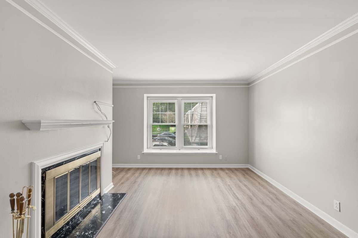 Spacious Living Room with a wood-burning fireplace, fresh paint, lots of natural light, and LVP flooring. Ached doorway and crown moulding offer an elevated feel to this peaceful space.