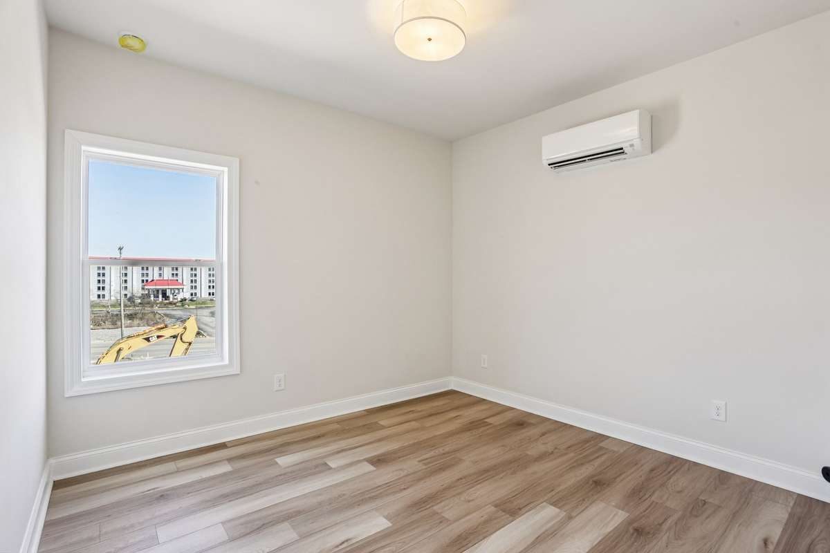 Comfortable bedroom featuring hardwood flooring, good natural light, and a dedicated wall-mounted HVAC unit.