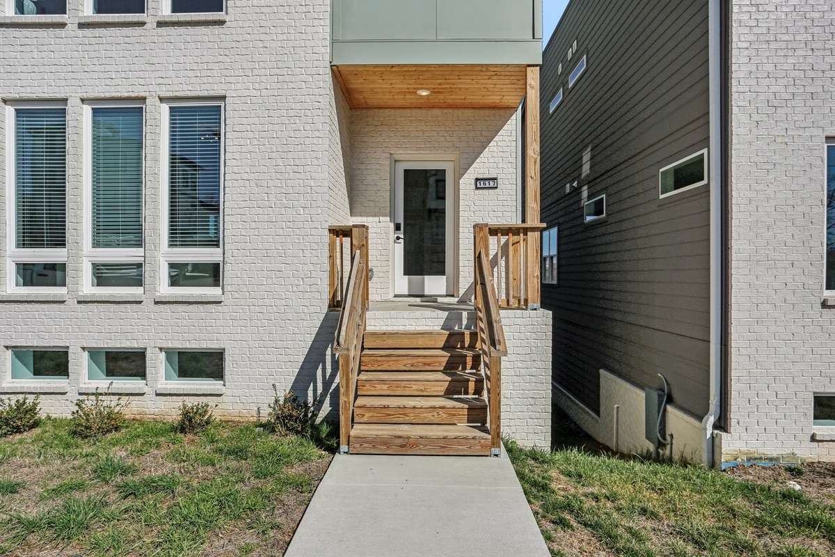Elevated front entry with wood steps and railing leading to a covered porch. Painted brick exterior and warm wood ceiling detail create a clean, contemporary look.