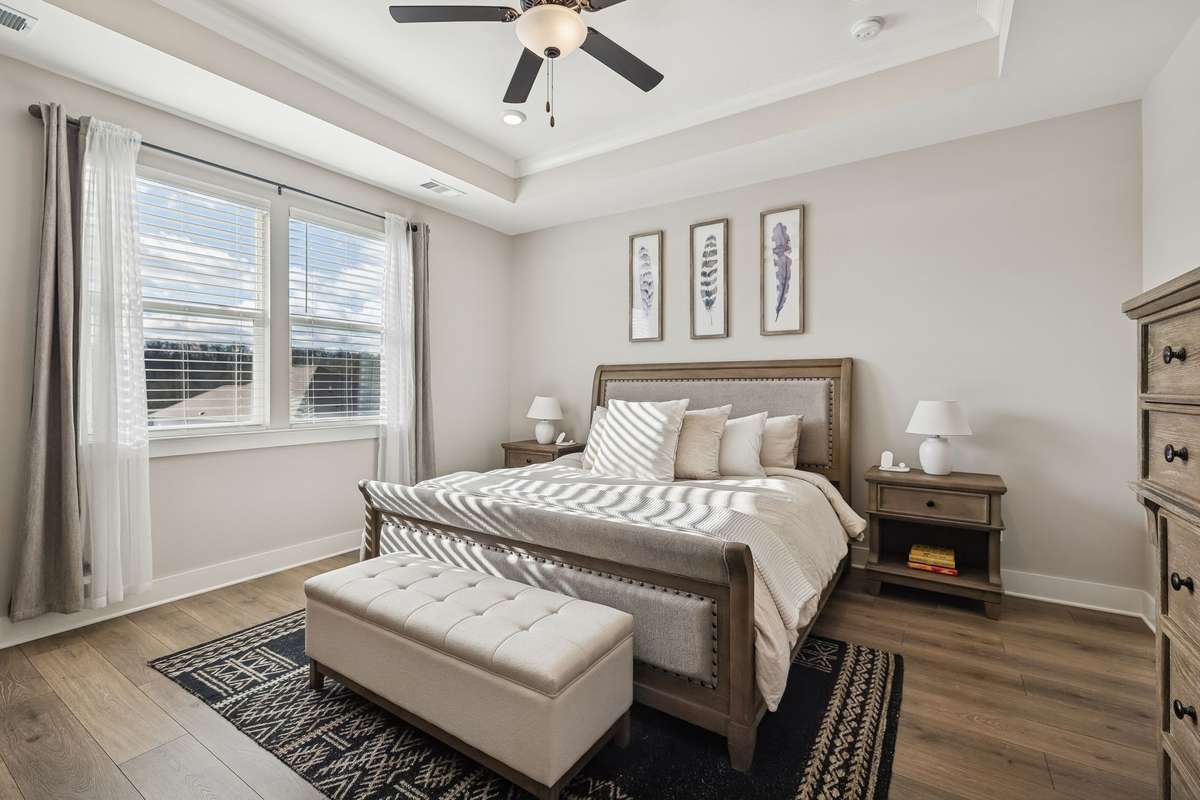 Primary suite with trey ceiling, ceiling fan, and natural lighting from the large windows.