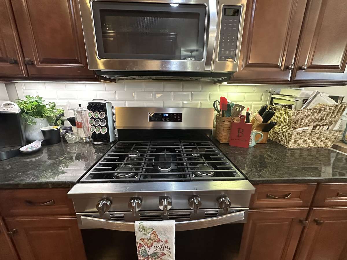 Gas stove/cooktop surrounded by granite countertops with tile backsplash and undercabinet lighting