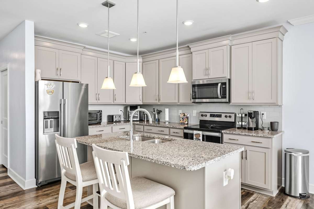 Bright, modern kitchen featuring granite countertops, stainless steel appliances, and abundant cabinetry. The spacious island with seating and stylish pendant lighting creates the perfect space for cooking, dining, and entertaining.