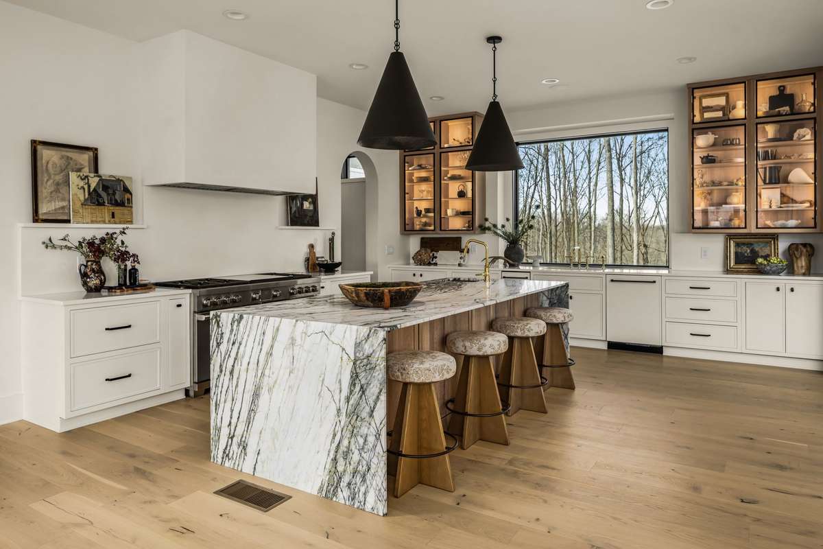 Gourmet kitchen featuring a dramatic marble island with waterfall edges, custom cabinetry, premium appliances, and abundant natural light, thoughtfully designed for both everyday living and elevated entertaining.