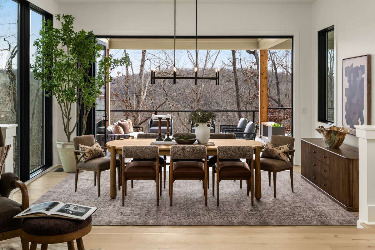 Dining area with fully opened glass doors, creating a seamless indoor-outdoor connection and extending the living space to the covered terrace with tranquil wooded views.