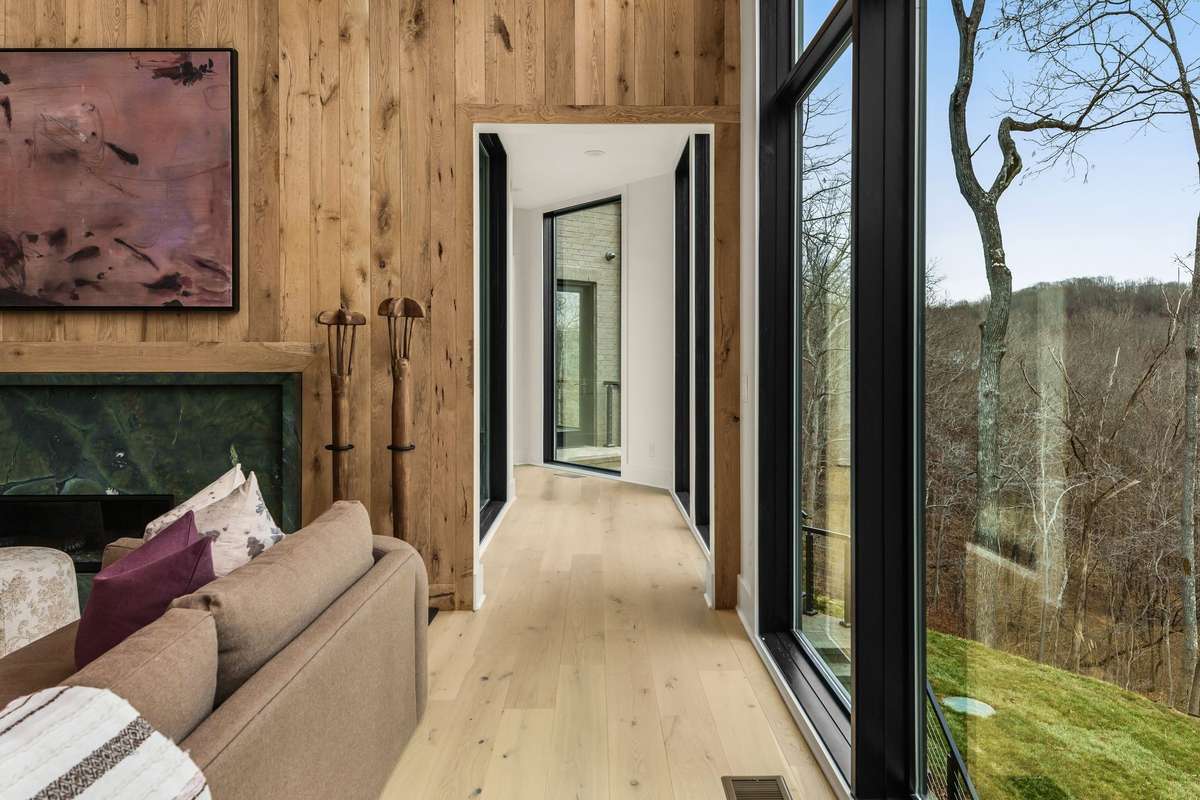 Gallery style hallway leading to the primary suite, framed by warm wood detailing and expansive windows that capture serene views and natural light.