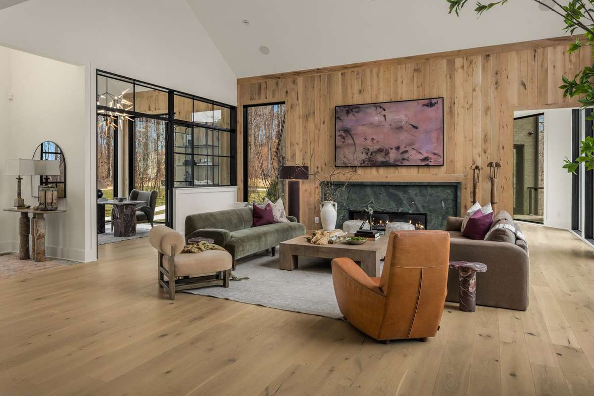 Living room featuring soaring vaulted ceilings, a statement fireplace, and expansive windows that fill the space with natural light while framing peaceful wooded views.